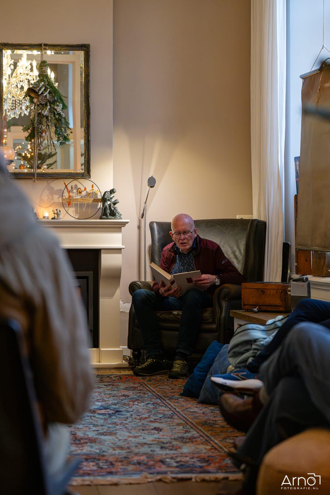 Voorlezer met boek in een leunstoel bij de haard